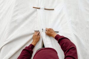 A person in a hoodie pushing a pin into the fabric above the doorway of a teepee